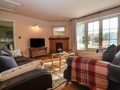 A living room with sofas a coffee table a fireplace and large windows at Rookery Cottage in Kelsale near Saxmundham