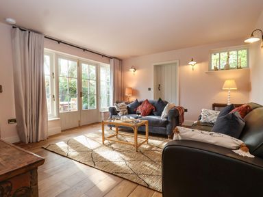 A living room with two sofas a glass coffee table and large windows at Rookery Cottage in Kelsale near Saxmundham