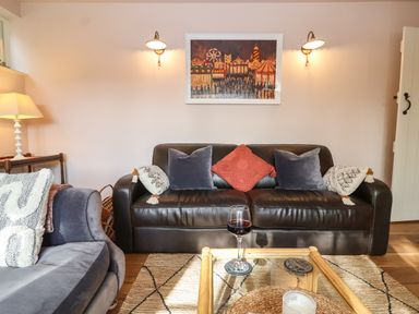 A living room with a black leather sofa with pillows a glass coffee table and a grey armchair at Rookery Cottage in Kelsale near Saxmundham
