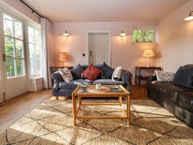 A living room with two sofas a glass coffee table and lamps at Rookery Cottage in Kelsale near Saxmundham