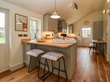 A kitchen with wooden floors a breakfast bar with stools and a table with bench seating at Rookery Cottage Kelsale near Saxmundham