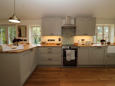 A kitchen with grey cabinets wooden countertops an oven a stainless steel range hood and windows at Rookery Cottage in Kelsale near Saxmundham
