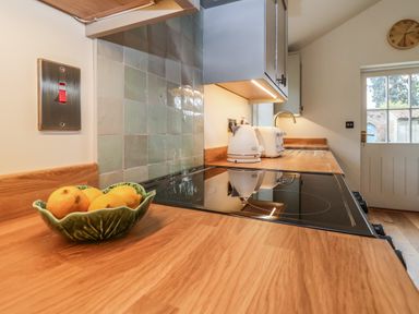 A kitchen counter with a green bowl of lemons an electric stove white kettle and toaster with a door and clock in the background at Rookery Cottage in Kelsale near Saxmundham