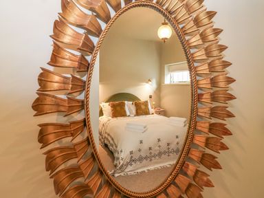 A bedroom with a bed reflected in an oval mirror with a decorative frame at Rookery Cottage in Kelsale near Saxmundham