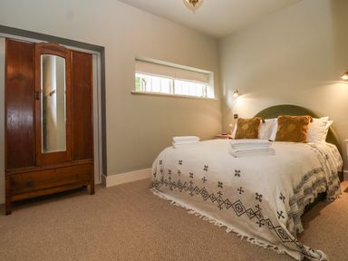 A bedroom with a bed covered with a patterned blanket pillows and folded towels two bedside tables with lamps and a wooden wardrobe with a mirror at Rookery Cottage in Kelsale near Saxmundham