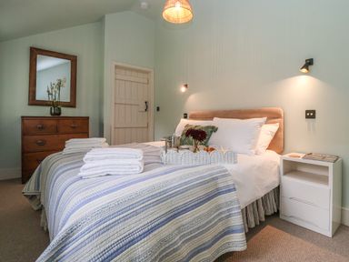 A bedroom with a bed covered in striped blue and white bedding a wooden dresser with a mirror and a white nightstand at Rookery Cottage in Kelsale near Saxmundham