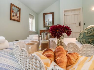 A bedroom with a tray holding croissants mugs a coffee pot and flowers on the bed at Rookery Cottage in Kelsale near Saxmundham