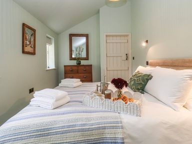 A bedroom with a bed with a tray of breakfast items and towels on a striped bedspread at Rookery Cottage in Kelsale near Saxmundham