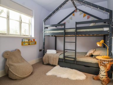 A child's bedroom with a dark bunk bed shaped like a house a yellow lamp on a tiger-shaped side table a furry beige chair and a yellow wall-mounted bookshelf at Rookery Cottage in Kelsale near Saxmundham