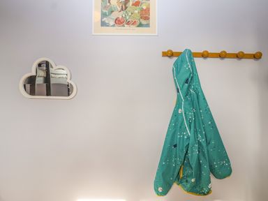 A wall with a cloud-shaped mirror a framed picture and a coat hanging on a wooden peg rail at Rookery Cottage in Kelsale near Saxmundham