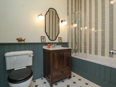 A bathroom with a toilet a wooden vanity with sink a mirror and a bathtub with striped tiles at Rookery Cottage in Kelsale near Saxmundham