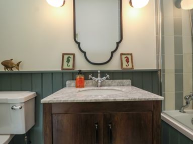 A bathroom with a wooden vanity and marble countertop a mirror two framed seahorse pictures and a bathtub at Rookery Cottage in Kelsale near Saxmundham