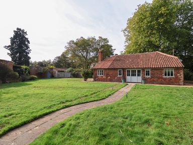 A brick cottage with a tiled roof and a paved pathway through a grassy garden at Rookery Cottage in Kelsale near Saxmundham