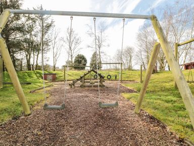 A playground with swings and climbing equipment surrounded by grass and trees at Matfen in Longframlington
