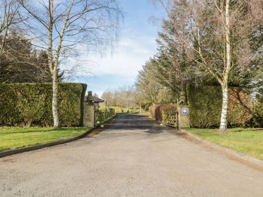 A driveway entrance with open wooden gates flanked by brick pillars and trimmed hedges at Matfen in Longframlington
