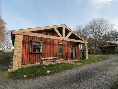 A wooden cabin with stone pillars and a picnic bench outside at Matfen in Longframlington