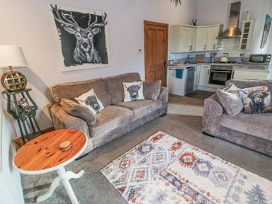 A living room with two sofas and a wooden round table next to a kitchen area with white cabinets at Matfen in Longframlington