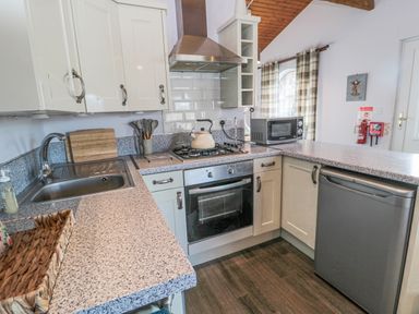 A kitchen with a sink and drying rack a stove with an oven a microwave a dishwasher and kitchen cabinets at Matfen in Longframlington