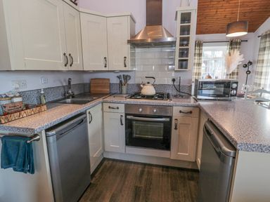 A kitchen with white cabinets a gas stove oven two dishwashers a microwave and a sink at Matfen in Longframlington