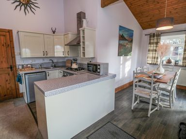 A kitchen with white cabinets a dining table and chairs next to a window at Matfen in Longframlington