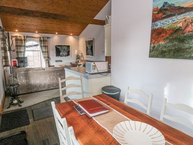 A dining table with chairs and a plate next to a living room with a sofa and artwork at Matfen in Longframlington