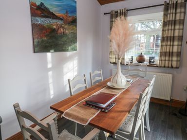 A dining room with a wooden table and chairs a vase with pampas grass on the table and a window with plaid curtains at Matfen in Longframlington
