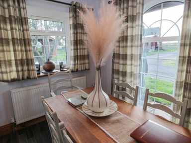 A dining room with wooden table white chairs a large vase with pampas grass and windows with curtains at Matfen in Longframlington