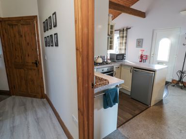 A kitchen with appliances and a countertop next to a hallway with wooden door and picture frames at Matfen in Longframlington