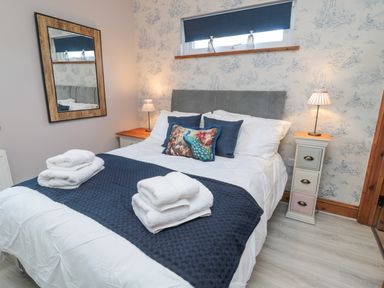 A bedroom with a double bed with pillows and folded towels bedside tables with lamps and a mirror on the wall at Matfen in Longframlington