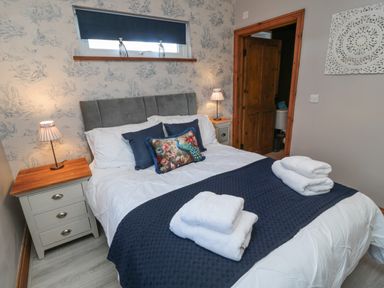 A bedroom with a bed with white and blue bedding and folded towels on the bed bedside tables with lamps and a window at Matfen in Longframlington