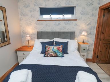 A bedroom with a double bed blue and floral pillows and bedside tables with lamps at Matfen in Longframlington
