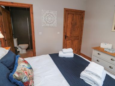A bedroom with a neatly made bed with towels on it a floral pillow wooden doors and a dresser with items on it at Matfen in Longframlington