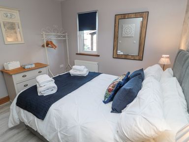 A bedroom with a bed with white bedding and blue pillows a dresser a clothes rack and a window at Matfen in Longframlington