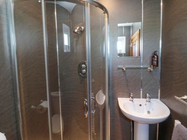 A bathroom with a corner shower enclosure a pedestal sink a mirror and a bottle on a glass shelf at Matfen in Longframlington