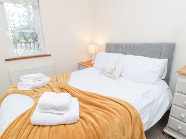 A bedroom with a bed covered in white linens and a mustard blanket a bedside table with a lamp and a window with glass bottles on the sill at Matfen in Longframlington