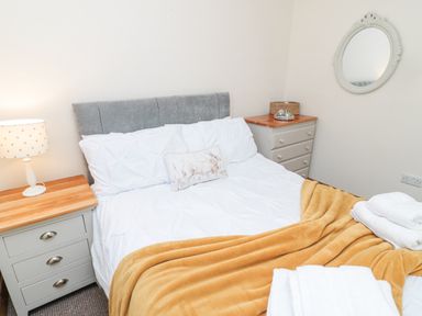 A bedroom with a bed with white bedding and a mustard blanket with bedside tables and a round mirror on the wall at Matfen in Longframlington