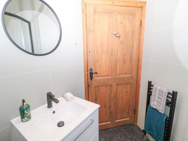A bathroom with a wooden door a white sink with a black faucet a round mirror and a black towel rack with two towels at Matfen in Longframlington