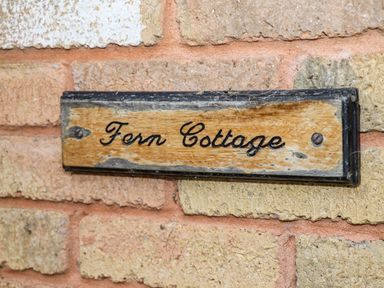 A wooden sign with the text Fern Cottage mounted on a brick wall at Fern Cottage in St Brides-Super-Ely