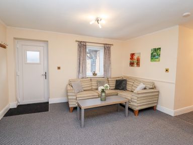 A living room with a striped corner sofa cushions a coffee table flowers on the table paintings on the wall at Fern Cottage in St Brides-Super-Ely