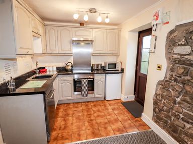 A kitchen with tiled floor stone wall cabinets oven sink microwave and a door at Fern Cottage in St Brides-Super-Ely