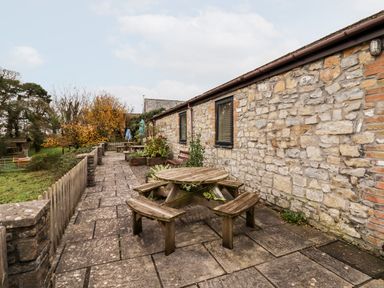 A stone patio with round wooden picnic tables and benches next to a stone building at Fern Cottage in St Brides-Super-Ely