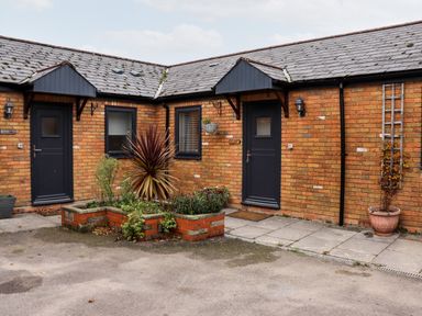 A brick courtyard with two black doors windows and planted flower beds at Fern Cottage in St Brides-Super-Ely