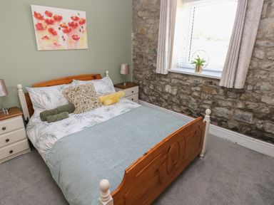 A bedroom with a wooden bed and patterned bedding stone wall window with curtains and nightstands with lamps at Fern Cottage in St Brides-Super-Ely