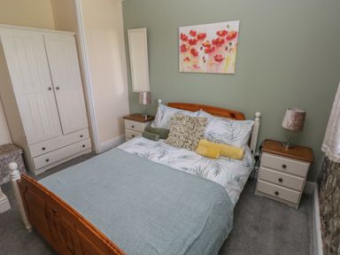 A bedroom with a wooden bed a wardrobe two bedside tables with lamps and a floral painting on the wall at Fern Cottage in St Brides-Super-Ely