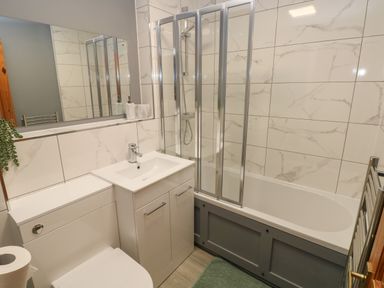 A bathroom with a toilet sink vanity bathtub with glass shower screen and towel radiator at Fern Cottage in St Brides-Super-Ely