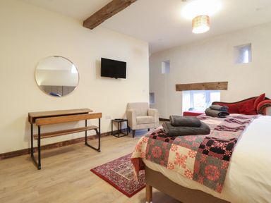 A bedroom with a bed, chair, table, and wall-mounted TV at Godre'r Gyrn, Plas Moelfre Hall Barns, Oswestry