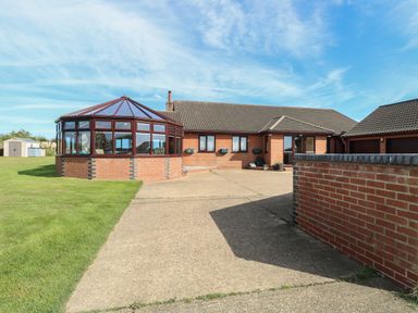 A driveway leading to a brick house with a glass conservatory and a double garage at Beach Haven in Happisburgh East Anglia