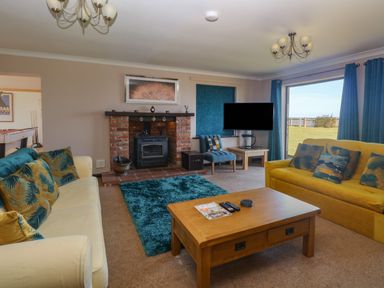 A living room with sofas and cushions around a wooden coffee table and a brick fireplace at Beach Haven in Happisburgh East Anglia