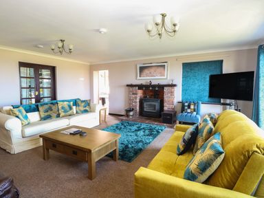 A living room with a yellow sofa and a white sofa with cushions a wooden coffee table a blue rug a brick fireplace a blue armchair and a wall-mounted TV at Beach Haven in Happisburgh East Anglia