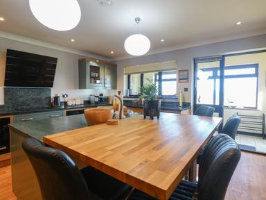 A kitchen with wooden dining table surrounded by black chairs and green cabinetry at Beach Haven in Happisburgh East Anglia